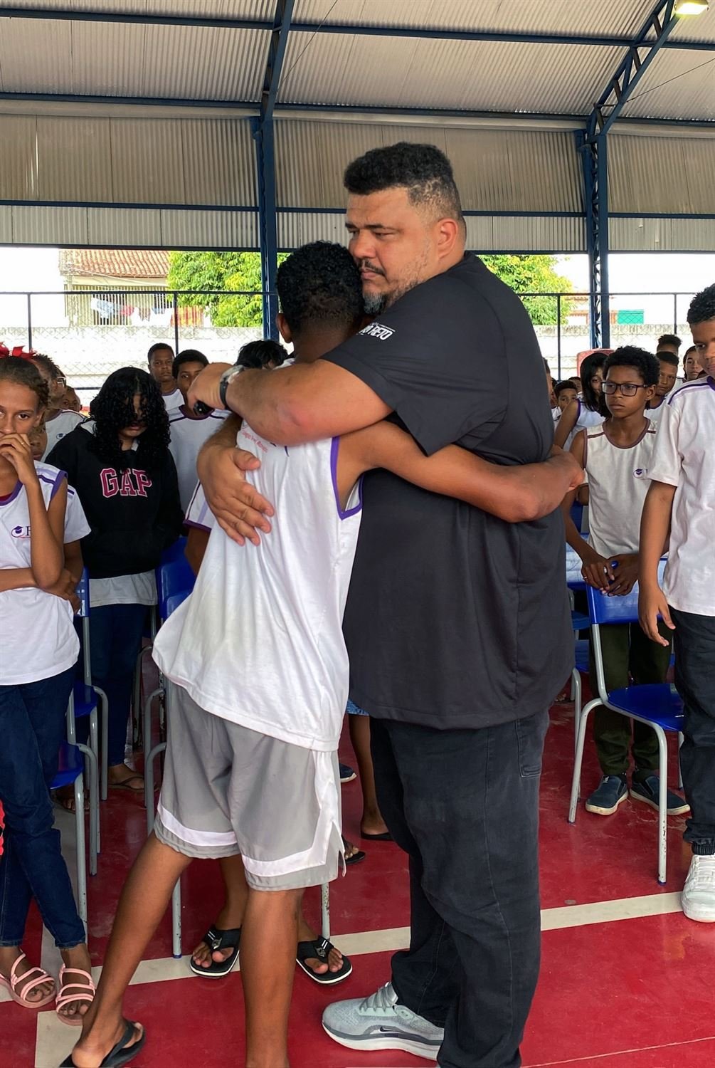 Educador do Instituto Papo Reto abraçando um adolescente durante uma ação em escola